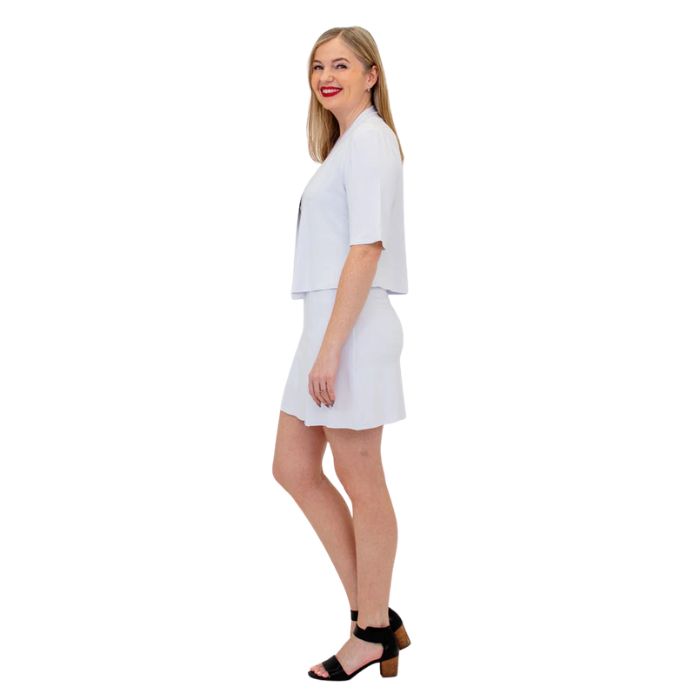 female model wearing white doda jacket, black avalon tank top and white melly skort side view on white background